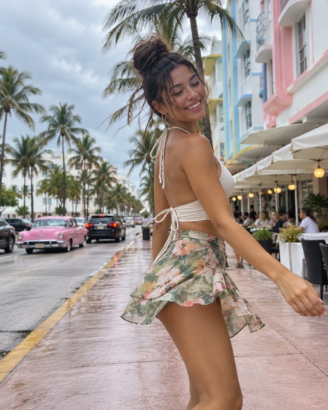 A smiling young woman with a messy top bun in a white halter top and floral skirt twirls on the Ocean Drive sidewalk in South Beach, pastel Art Deco hotels, palm trees and a pink vintage car behind her: Rockstarr Media is casting new faces in Miami