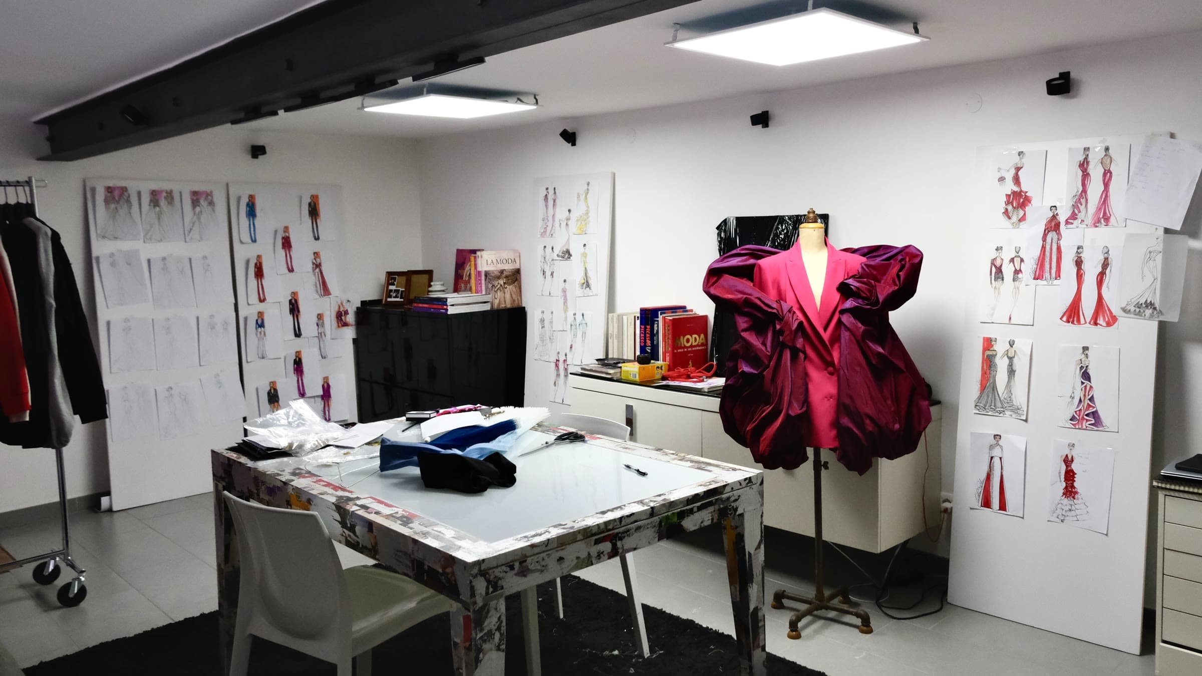 Fashion designer's studio with a hot pink sculptural design on a dress form and fashion sketches on the wall: Rockstarr Media Fashion Show 2027 call for designers